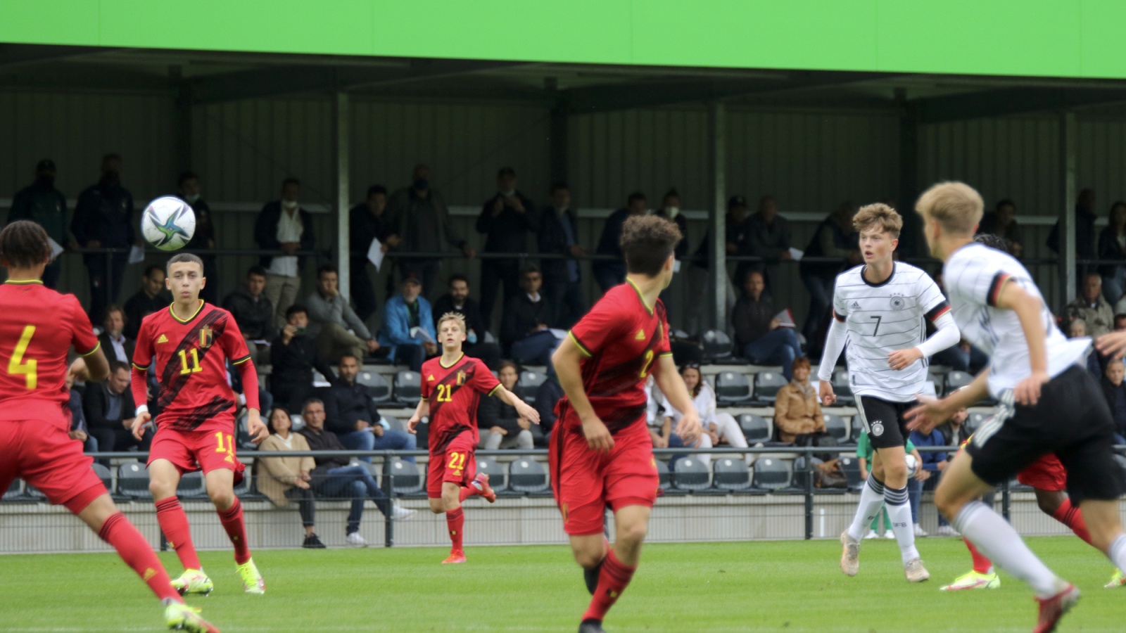 Fußballspiel: Belgien (rot) gegen Deutschland (schwarz/weiß). Spieler mit Ball in der Spielmitte, Zuschauerreihen im Hintergrund.
