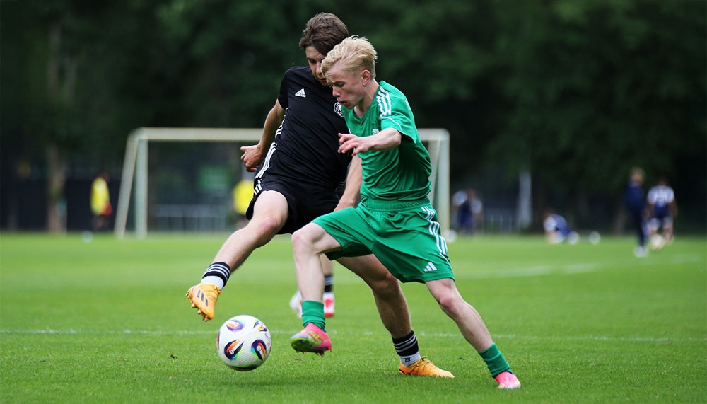 [{"clang_id":1,"value":"Zwei Fußballspieler im Zweikampf auf grünem Rasen. Links ein Spieler in schwarzem Trikot, rechts in grünem. Beide versuchen, den Ball zu erobern."}]