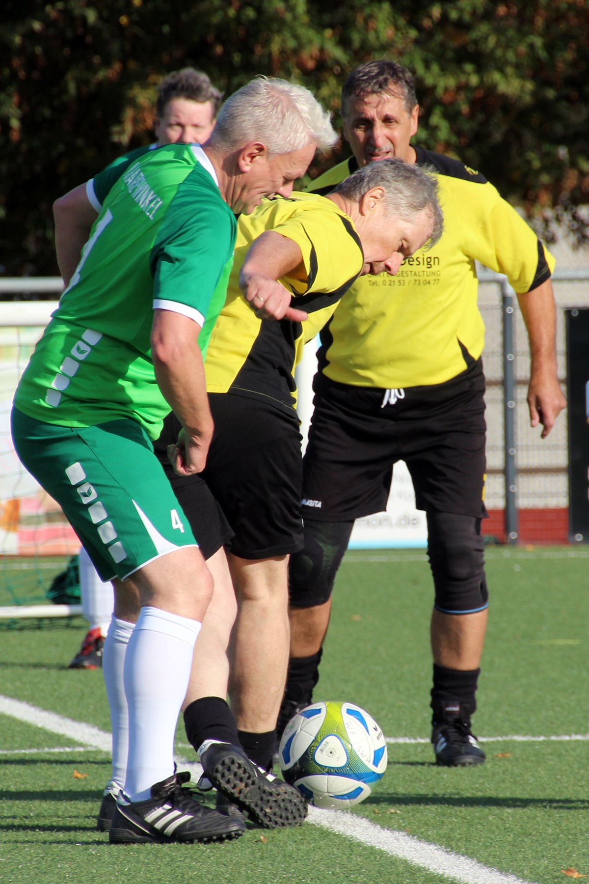 [{"clang_id":1,"value":"Drei Fußballspieler stehen auf einem grünen Rasenfeld. Ein Spieler in Grün und Schwarz versucht, den Ball vom Spieler in Gelb zu erobern."}]