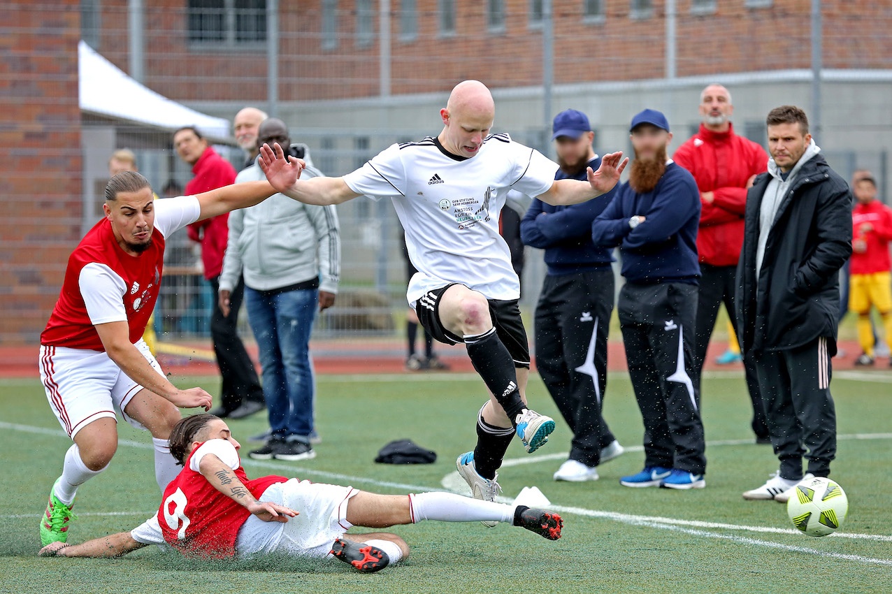 [{"clang_id":1,"value":"Fußballspiel: Spieler in rot und weiß kämpfen um Ball. Im Hintergrund Zuschauer und Zäune. Ein Spieler liegt am Boden."}]