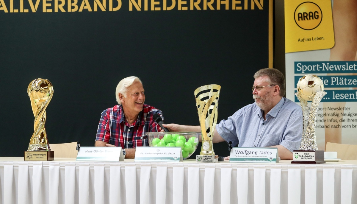 [{"clang_id":1,"value":"Fünf Männer sitzen an einem Tisch mit Pokalen und einer Tennisball-Figur. Im Hintergrund ein Banner mit Schriftzug und Logo."}]