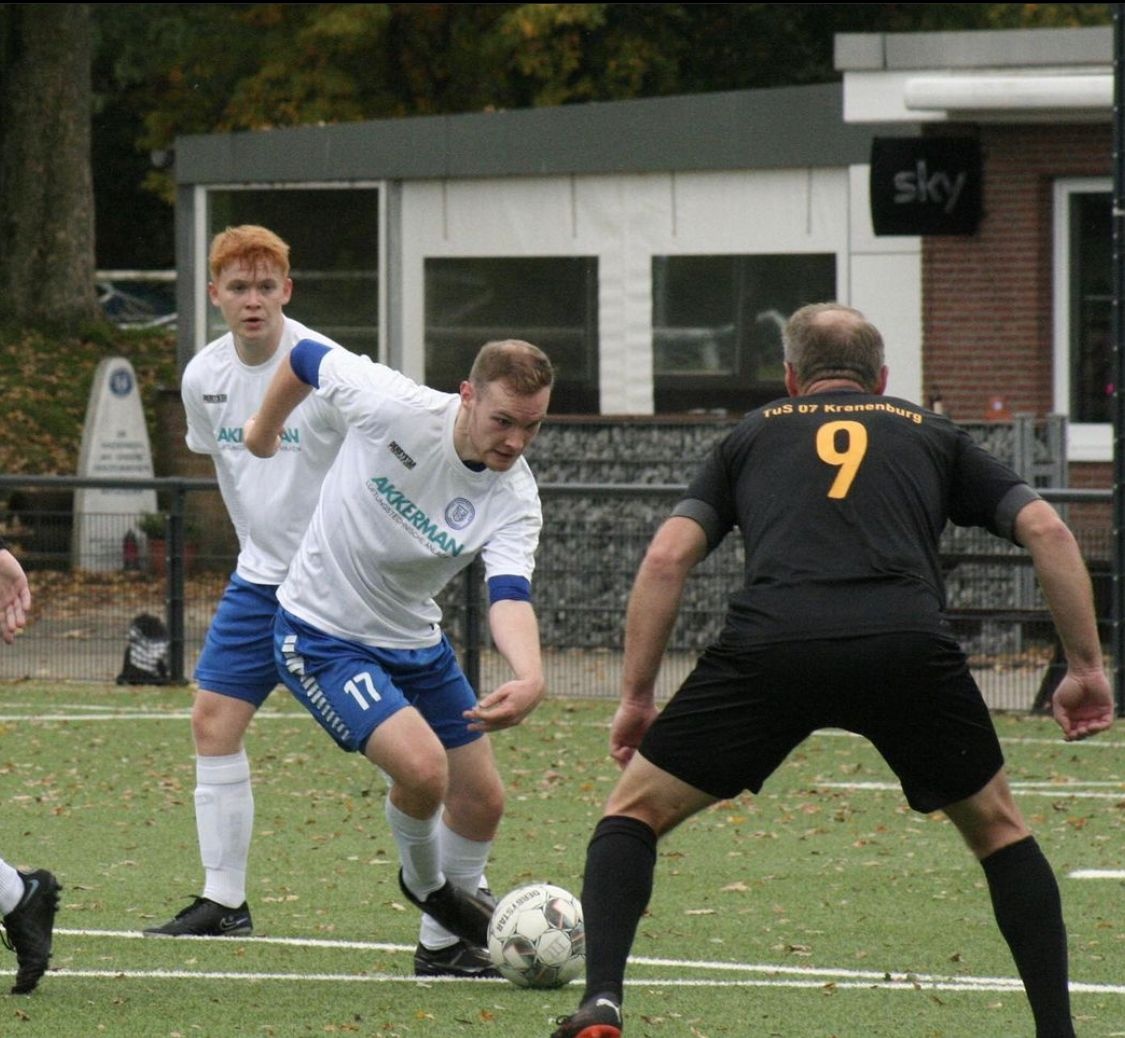 [{"clang_id":1,"value":"Fußballspiel: Zwei Spieler in weißen Trikots und blauen Shorts umdribbeln einen Spieler in schwarzem Trikot mit Nummer 9. Rasenplatz, Gebäude im Hintergrund."}]