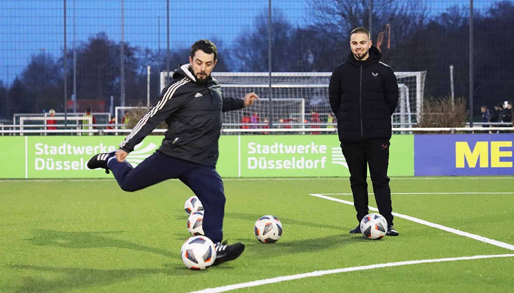 [{"clang_id":1,"value":"Zwei Männer auf Fußballfeld. Links dribbelt einer den Ball, rechts steht der andere. Im Hintergrund Tor und Werbebanner."}]