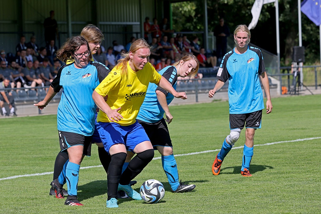 [{"clang_id":1,"value":"Fußballspiel: Vier Spielerinnen kämpfen um den Ball auf dem Rasen. Eine trägt Gelb-Blau, die anderen Hellblau-Schwarz. Im Hintergrund Zuschauer."}]
