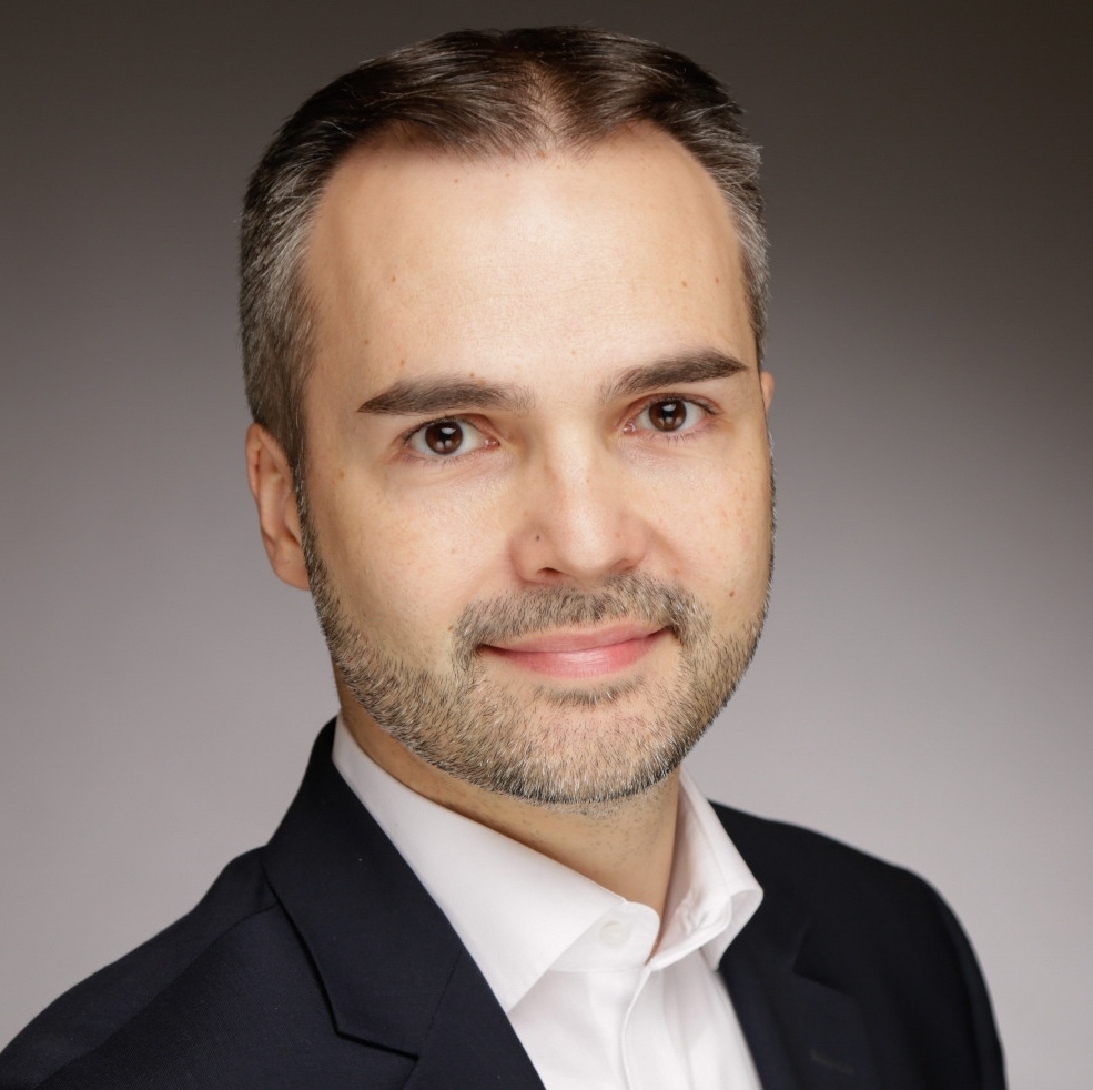 [{"clang_id":1,"value":"Mann mit grau meliertem Haar und Bart, gekleidet in weißen Hemdkragen und schwarzen Blazer, vor grauem Hintergrund."}]