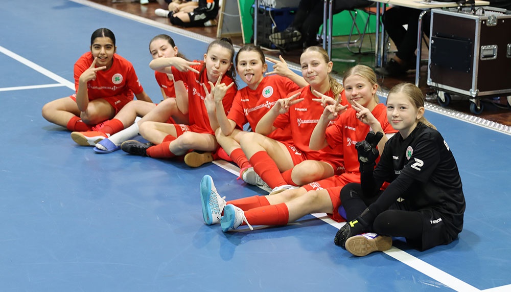 [{"clang_id":1,"value":"Handballteam sitzt auf blauem Hallenboden. Sieben Spielerinnen in roten Trikots zeigen beide Daumen hoch. Eine Spielerin trägt dunkle Sportkleidung."}]