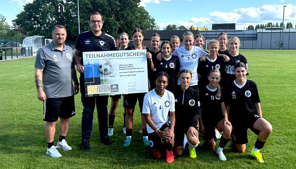 [{"clang_id":1,"value":"Fußballteam mit Trainer und Sponsoren auf Grünfeld. Im Hintergrund Fußballtor und Gebäude. Alle lächeln in die Kamera."}]