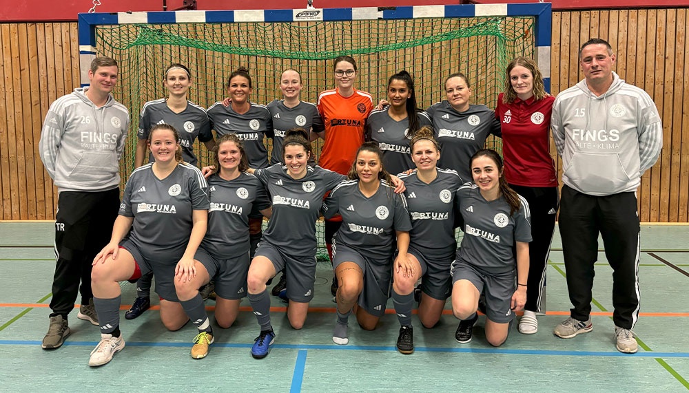 [{"clang_id":1,"value":"Futsal-Mannschaft, Frauen und Männer, in Sportkleidung vor einem Tor in einer Sporthalle. Alle lächeln in die Kamera."}]