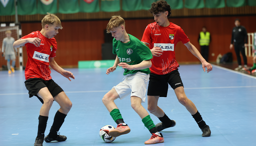 [{"clang_id":1,"value":"Drei Jugendliche spielen Futsal in einer Halle. Sie tragen rote und weiße Trikots mit schwarzen Shorts und Stutzen. Einer dribbelt den Ball."}]
