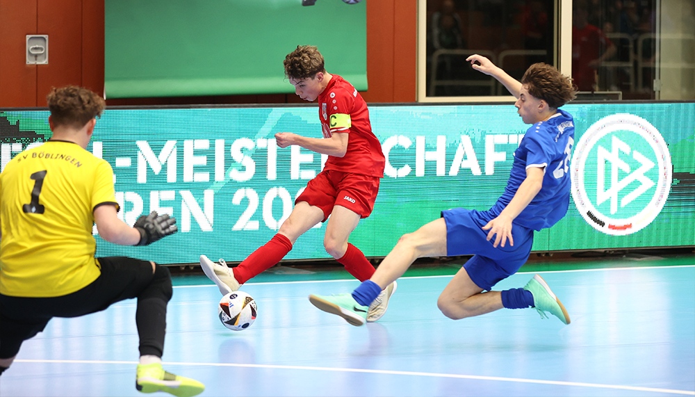 [{"clang_id":1,"value":"Handballspiel: Roter Spieler schießt, blauer Spieler springt zur Abwehr, gelber Spieler im Hintergrund. Halle mit Werbebanner im Hintergrund."}]