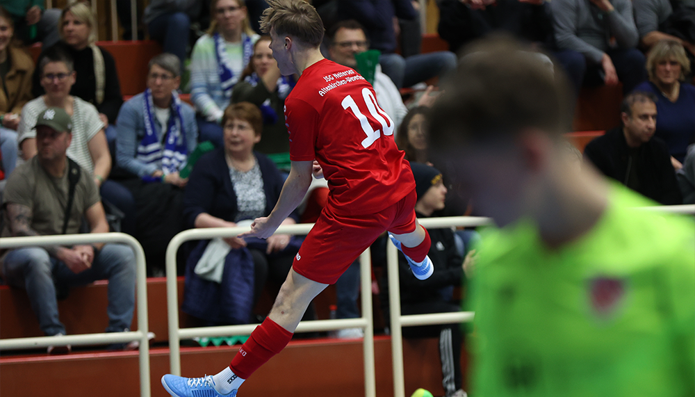 [{"clang_id":1,"value":"Handballspieler mit rotem Trikot und Nummer 19 in Aktion vor Zuschauern. Gegner in grün im Hintergrund verschwommen."}]