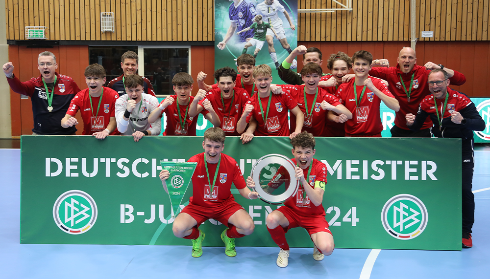 [{"clang_id":1,"value":"Handballmannschaft in roten Trikots mit Medaillen vor einem Banner mit der Aufschrift \"Deutscher B-Jugend Meister 2024\". Jubelnde Spieler und Trainer."}]