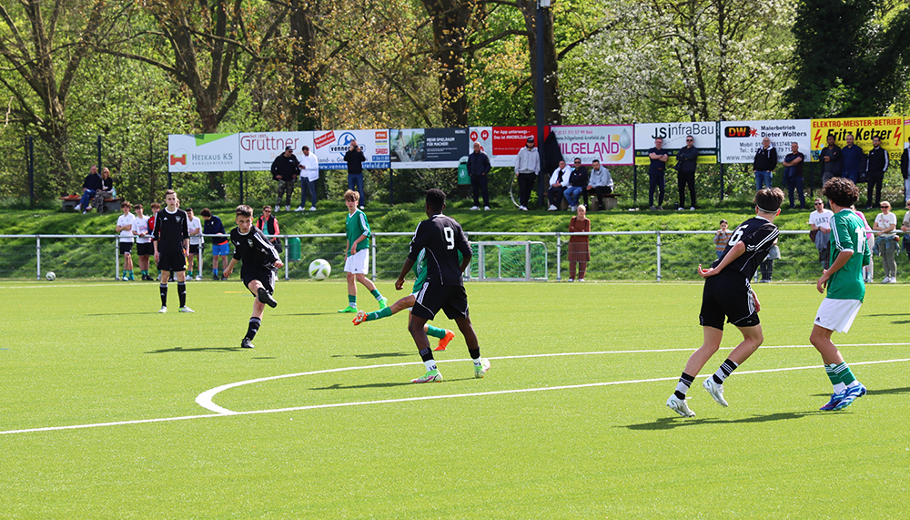 [{"clang_id":1,"value":"Fußballspiel auf grünem Rasen. Spieler in schwarzen und grünen Trikots kämpfen um den Ball. Im Hintergrund eine Zuschauertribüne mit Werbebannern."}]