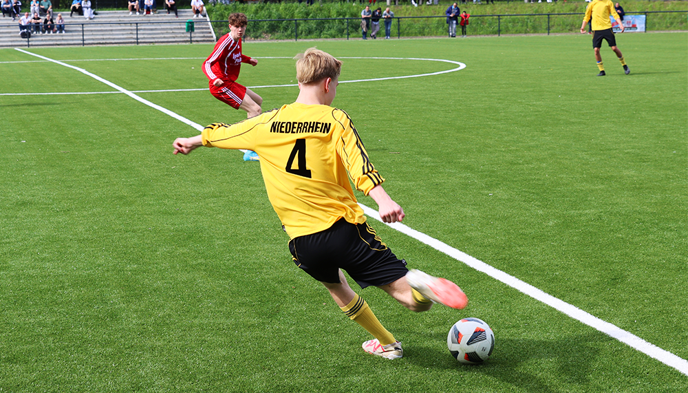 [{"clang_id":1,"value":"Fußballspieler mit gelbem Trikot und schwarzer Hose schießt auf ein Fußballfeld. Im Hintergrund sind weitere Spieler und Zuschauerränge zu sehen."}]