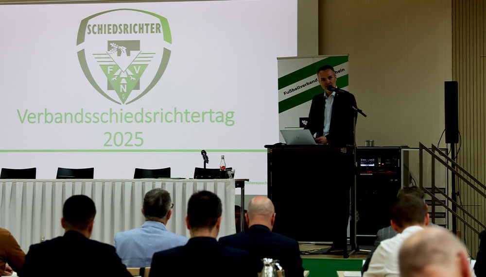 [{"clang_id":1,"value":"Raum mit Podium. Redner am Pult, dahinter Schriftzug \"Verbandschiedsrichtertages 2025\". Publikum sitzt vor dem Podium."}]