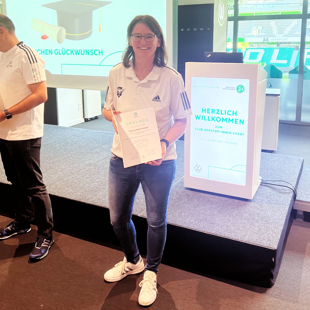 [{"clang_id":1,"value":"Frau mit Urkunde vor Werbeständer. Sie trägt Jeans, T-Shirt und Sneakers, lächelt in die Kamera. Im Hintergrund eine moderne Bürolandschaft."}]