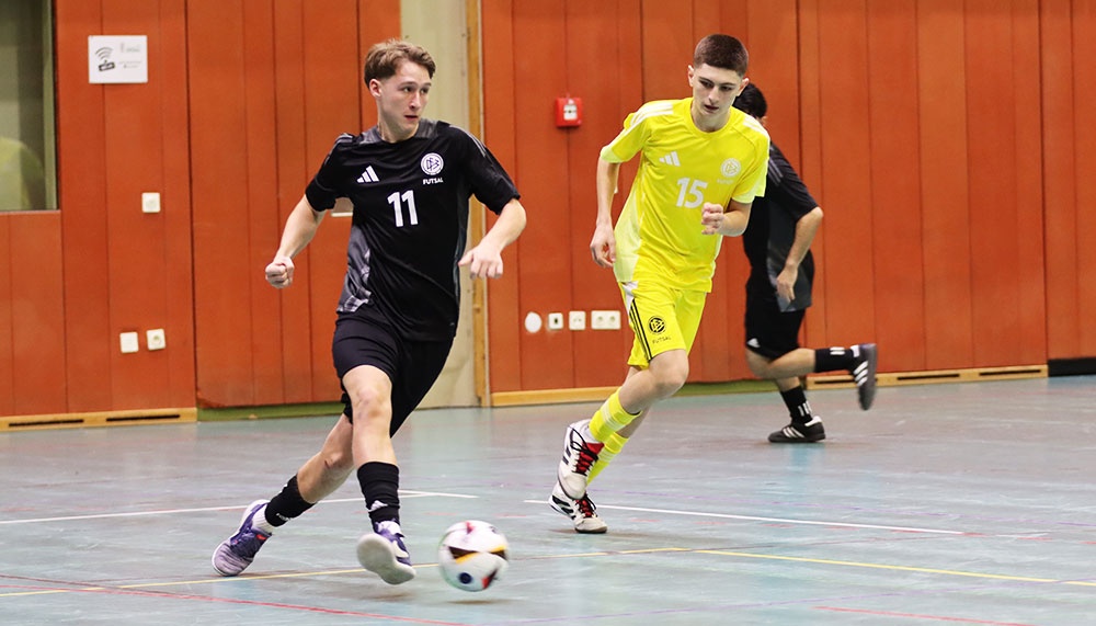 [{"clang_id":1,"value":"Futsal-Spiel in Sporthalle. Zwei Spieler im Vordergrund: links Spieler mit Nr. 11 in schwarzem Trikot, rechts Spieler mit Nr. 15 in gelbem Trikot."}]