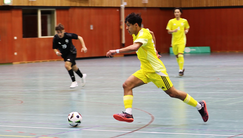 [{"clang_id":1,"value":"Futsal-Spiel in Sporthalle. Ein Spieler in gelbem Trikot dribbelt den Ball, verfolgt von einem Gegenspieler in schwarzem Trikot. Im Hintergrund ein weiterer Spieler in Gelb."}]