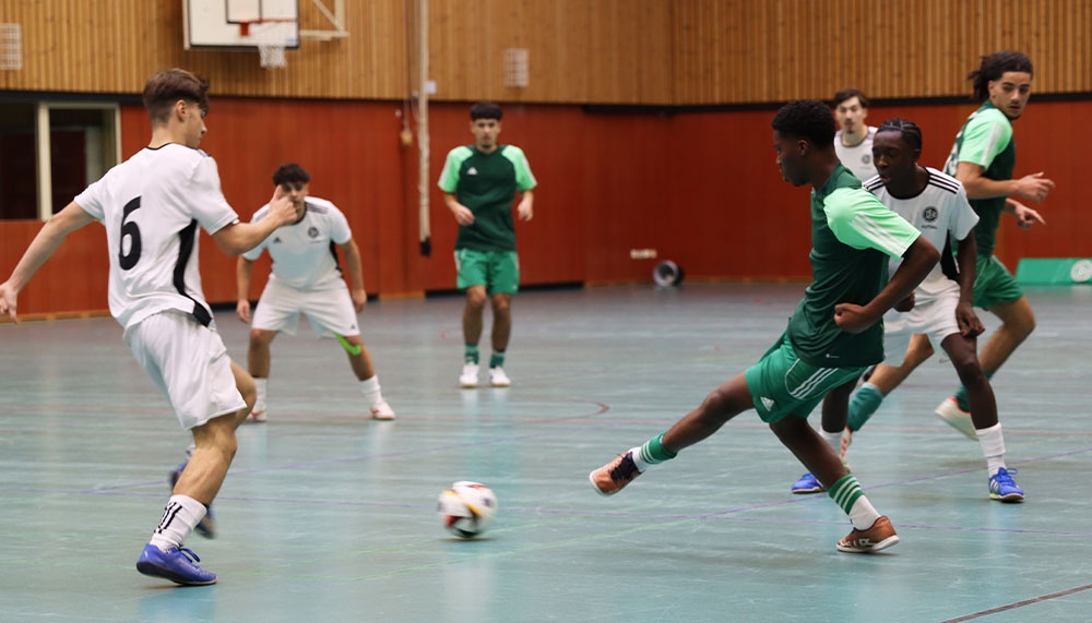 [{"clang_id":1,"value":"Futsalspiel in Sporthalle. Spieler in schwarzen und grünen Trikots kämpfen um Ball. Im Hintergrund weitere Spieler und Zuschauer."}]