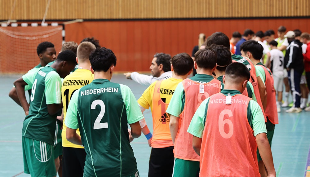 [{"clang_id":1,"value":"Futsal-Spieler mit Nummern auf den Trikots stehen sich auf einem Hallenfußballfeld gegenüber. Trikotfarben: Grün, Gelb, Orange. Im Hintergrund Zuschauer."}]