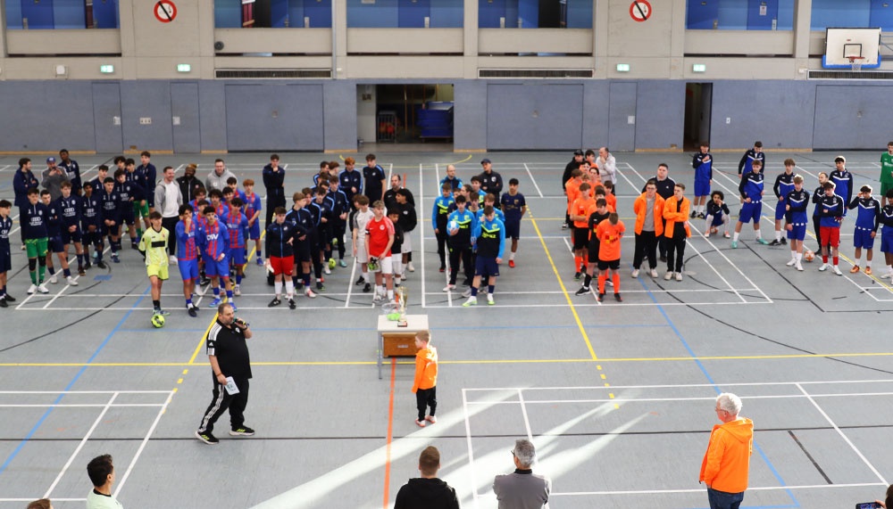 [{"clang_id":1,"value":"Sporthalle mit etwa 50 Kindern und Jugendlichen in Sportkleidung, die in zwei Gruppen aufgeteilt sind. Davor stehen Trainer und Betreuer."}]