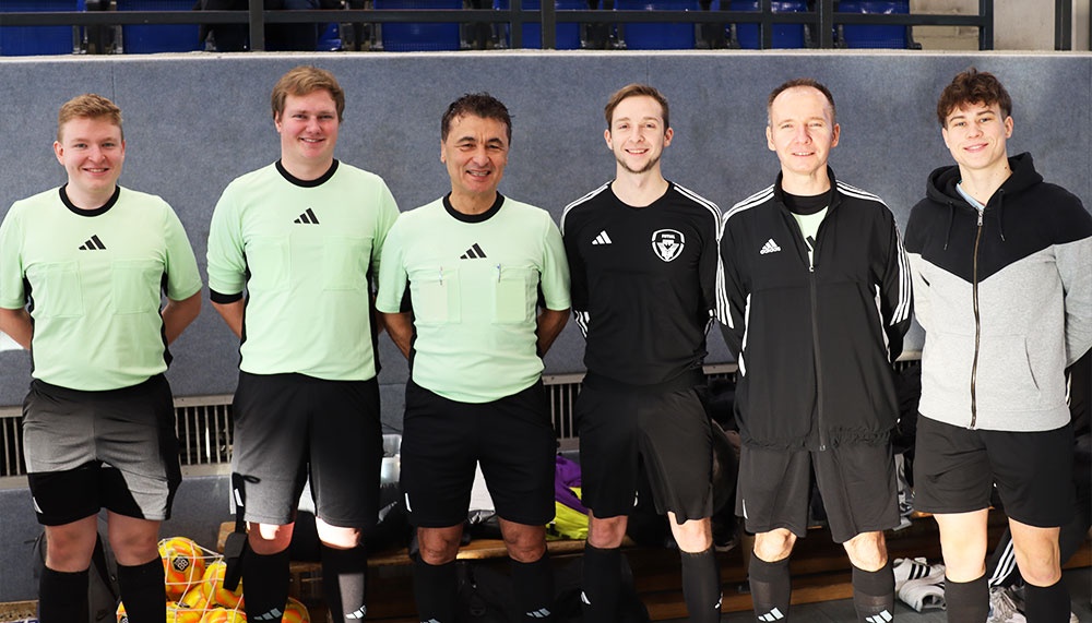 [{"clang_id":1,"value":"Sechs Männer in Sportkleidung stehen nebeneinander vor einer blauen Wand. Die meisten tragen Schiedsrichter- oder Fußballbekleidung."}]