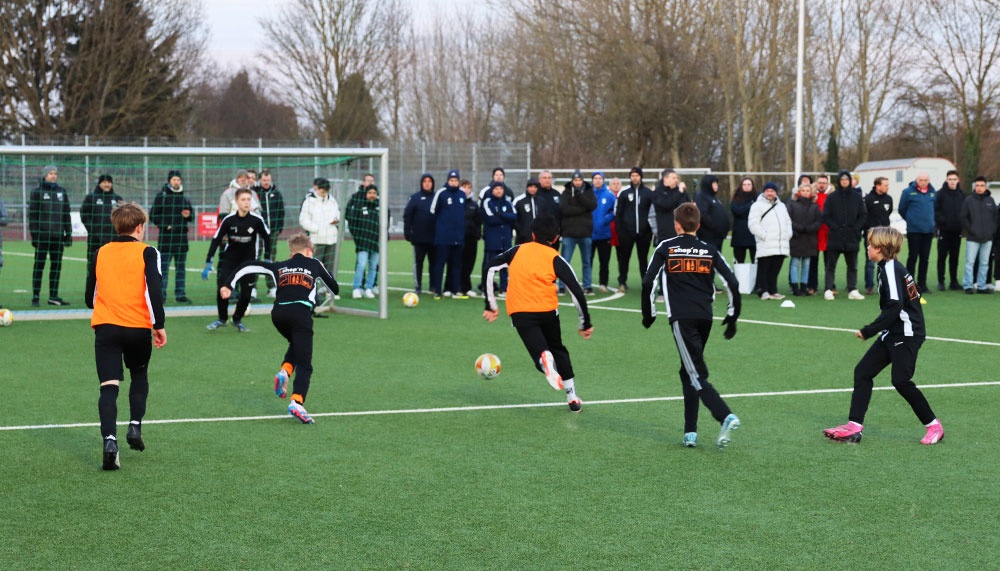 [{"clang_id":1,"value":"Fußballtraining mit Kindern und Jugendlichen auf einem Kunstrasenplatz. Zuschauer stehen am Spielfeldrand. Einige Spieler tragen orangefarbene Westen."}]