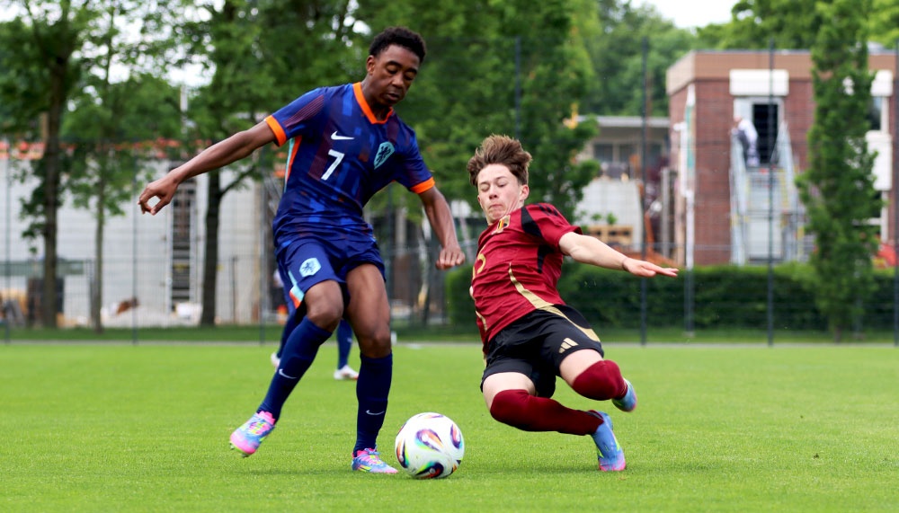 [{"clang_id":1,"value":"Zwei Fußballspieler auf grünem Rasen: Links ein Spieler mit blauem Trikot und Nummer 7, rechts ein Spieler mit rot-braunem Trikot bei Ballkontrolle."}]