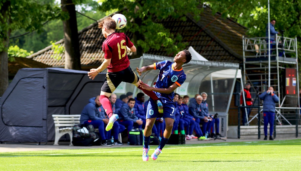 [{"clang_id":1,"value":"Zwei Fußballspieler springen im Luftkampf um den Ball. Im Hintergrund eine Zuschauertribüne und ein kleines Gebäude. Rasenplatz."}]
