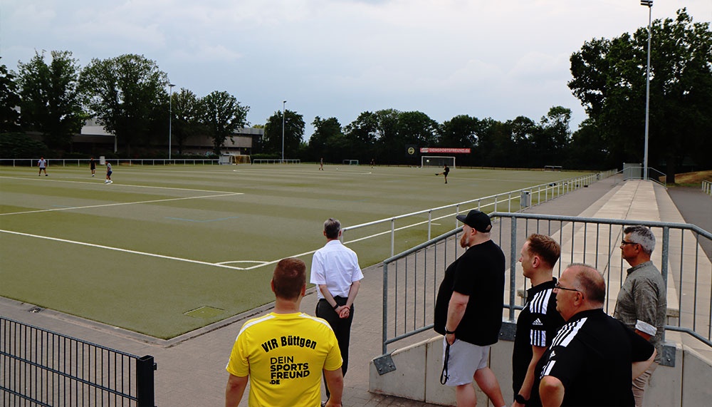 [{"clang_id":1,"value":"Fußballfeld mit Spielern. Am Rand stehen Zuschauer und ein Schiedsrichter. Im Hintergrund Bäume und Gebäude unter bewölktem Himmel."}]