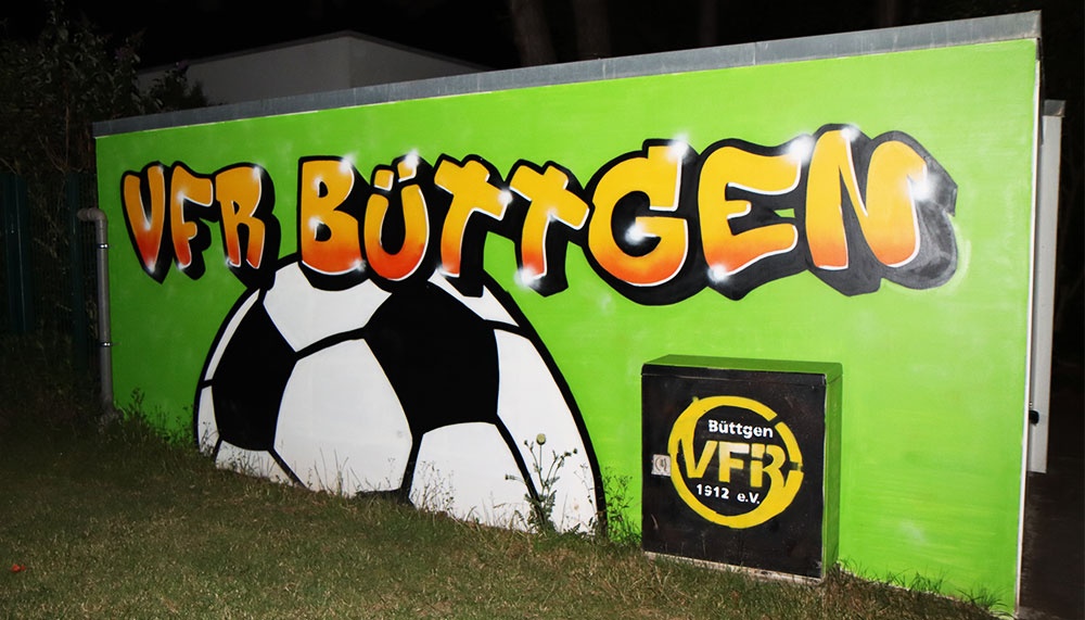 [{"clang_id":1,"value":"VFR Büttgen Vereinslogo und Schriftzug auf grünem Hintergrund. Darunter Fußball. Rahmen aus Metall. Rasen im Vordergrund."}]