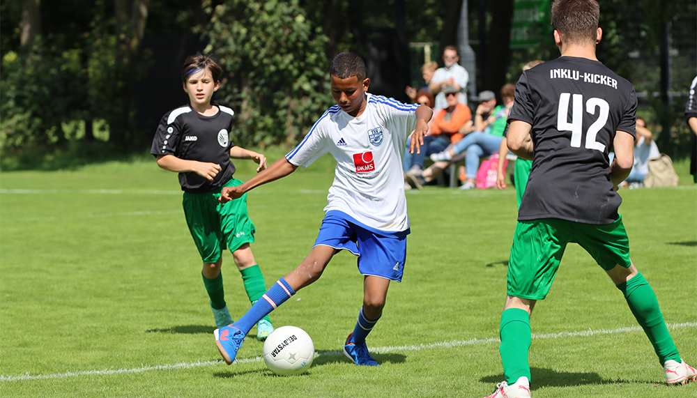 [{"clang_id":1,"value":"Drei Fussballspieler auf Grün. Ein Spieler in weissem Trikot schiesst auf das Tor, ein anderer in grünem Trikot rennt ihm entgegen. Im Hintergrund Zuschauer."}]