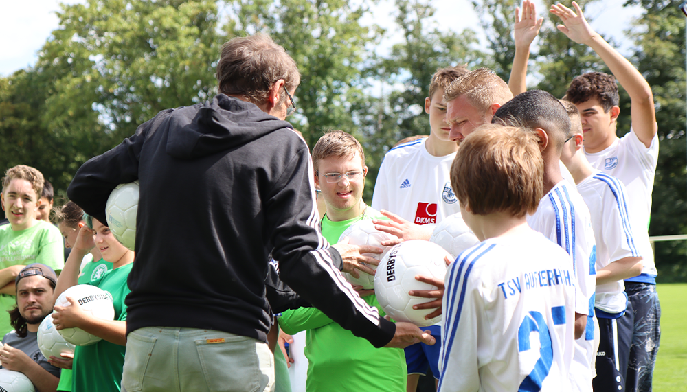 [{"clang_id":1,"value":"Fußballtrainer schüttelt Hand eines jungen Spielers. Im Hintergrund stehen weitere Jugendliche in Sportkleidung auf einem Fußballfeld."}]