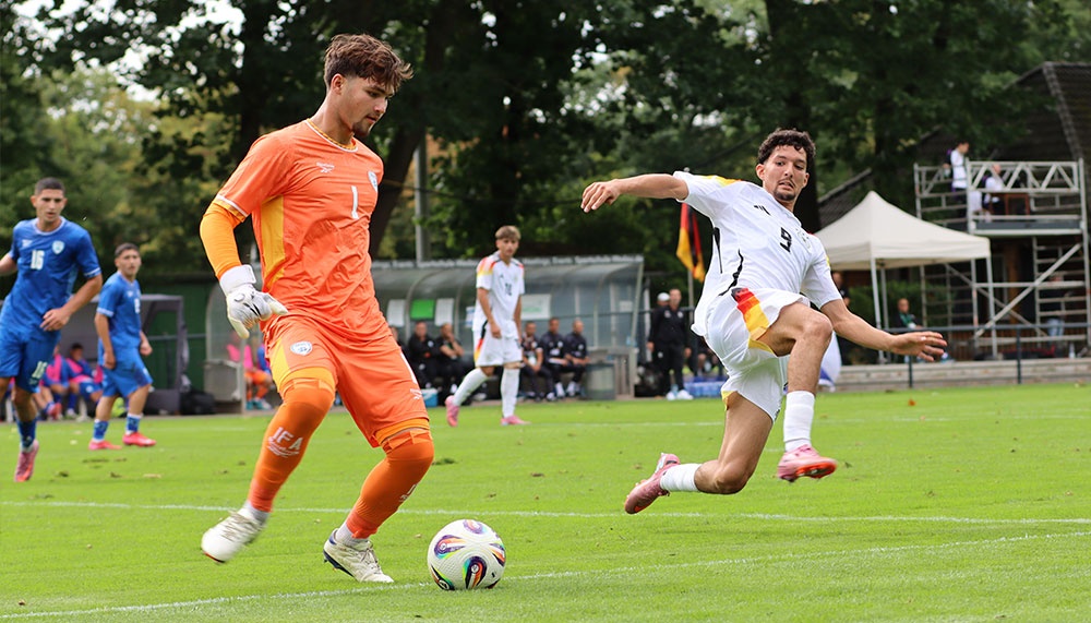 [{"clang_id":1,"value":"Fußballspiel: Torwart in orange wehrt Schuss eines Spielers mit Nummer 9 im weißen Trikot ab. Im Hintergrund weitere Spieler und Zuschauer."}]
