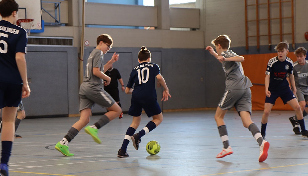 [{"clang_id":1,"value":"Fünf Jungen spielen Hallenfußball in einer Sporthalle. Ein Spieler mit Trikotnummer 10 dribbelt den Ball. Andere Spieler verteidigen oder bereiten sich auf den Angriff vor."}]