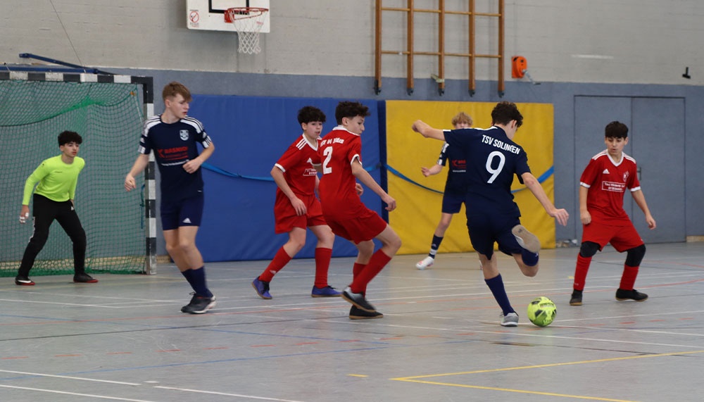 [{"clang_id":1,"value":"Futsalspiel in Sporthalle. Mehrere jugendliche Spieler in rot-weißem und blauem Trikot kämpfen um den Ball. Im Hintergrund ein Tor und Basketballkorb."}]