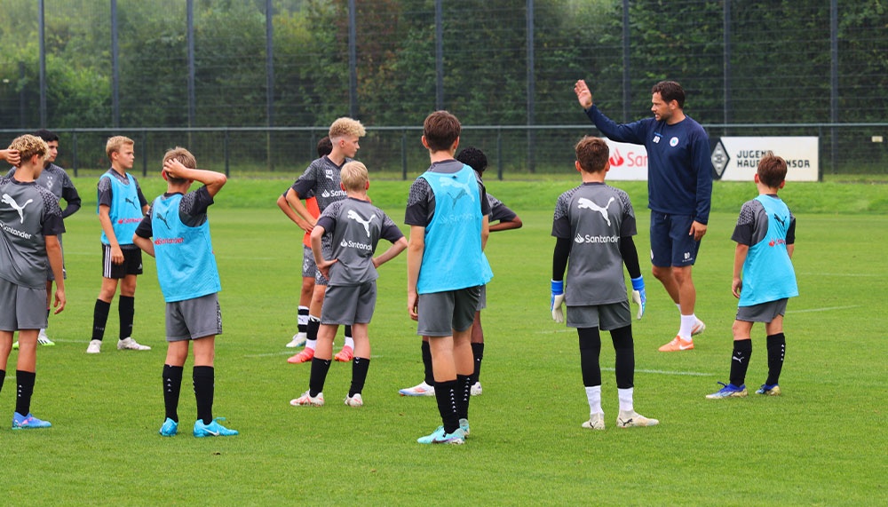 [{"clang_id":1,"value":"Fußballtraining: Gruppe Jugendlicher in Trainingsanzügen auf grünem Rasen, Trainer mit hochgehobener Hand gibt Anweisungen. Im Hintergrund eine Hecke."}]