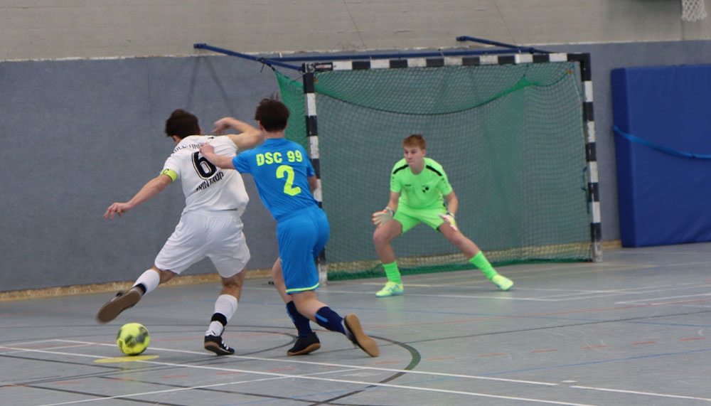 [{"clang_id":1,"value":"Futsal-Spiel in Sporthalle. Zwei Spieler in blau-weißem Trikot kämpfen um den Ball vor dem Tor. Dritter Spieler im Hintergrund."}]