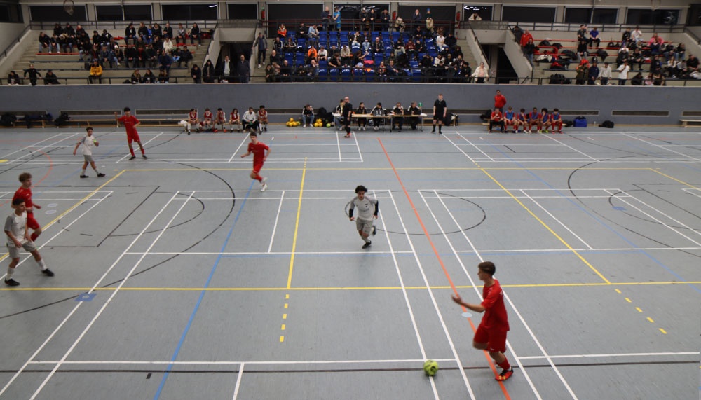 [{"clang_id":1,"value":"Futsalspiel in Sporthalle. Spieler in rot und weiß auf grauem Hallenboden mit Linien. Zuschauertribünen im Hintergrund."}]