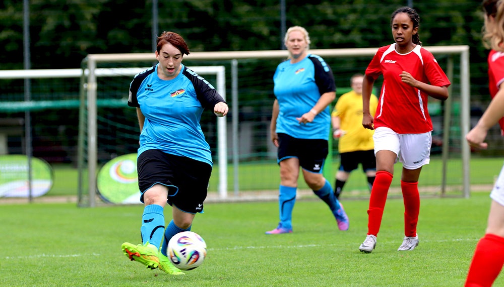 [{"clang_id":1,"value":"Fußballspiel: Eine Spielerin in blauem Trikot und schwarzen Shorts schießt auf das Tor. Im Hintergrund weitere Spielerinnen in unterschiedlichen Farben."}]