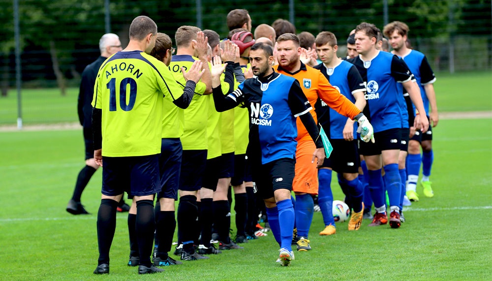 [{"clang_id":1,"value":"Fußballspiel: Spieler in gelben, blauen und orangefarbenen Trikots diskutieren mit dem Schiedsrichter auf dem grünen Rasen. Zuschauer im Hintergrund."}]