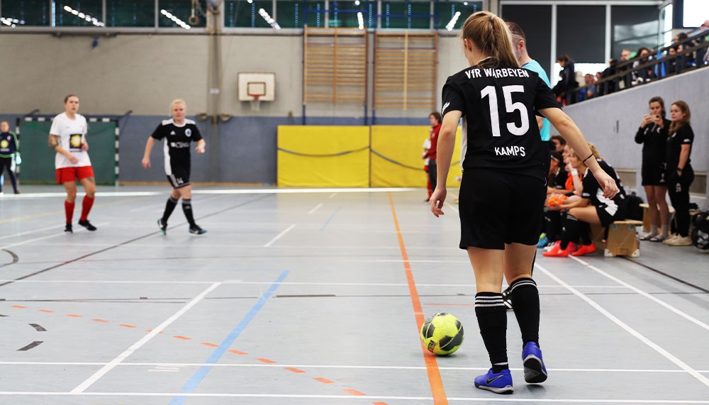 [{"clang_id":1,"value":"Handballspiel in Halle. Spielerin mit Nummer 15 dribbelt den Ball, weitere Spieler im Hintergrund. Zuschauerränge rechts."}]