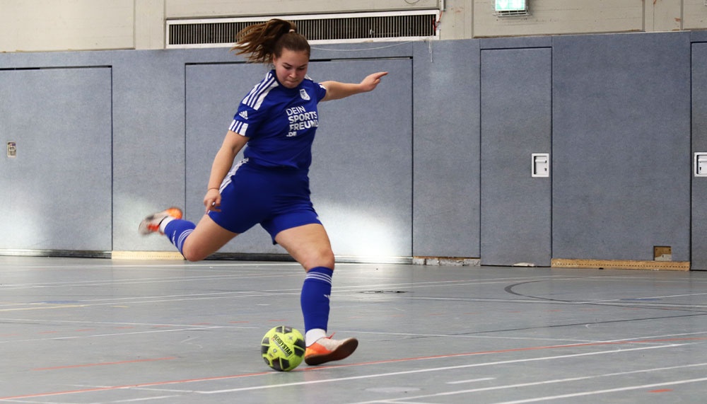 [{"clang_id":1,"value":"Fußballspielerin in blauem Trikot und Shorts schießt im Hallensportfeld auf einen Ball. Im Hintergrund graue Wand."}]