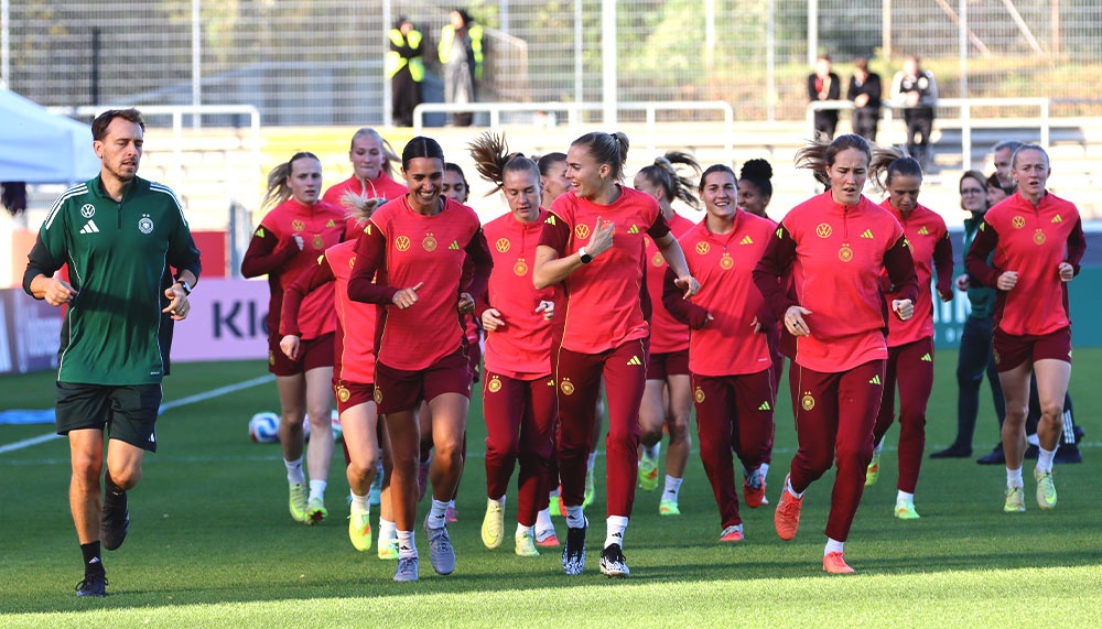 [{"clang_id":1,"value":"Fußballmannschaft in roten Trainingsanzügen läuft auf Rasenplatz zu. Trainer in grün begleitet sie. Im Hintergrund Stadiontribüne."}]