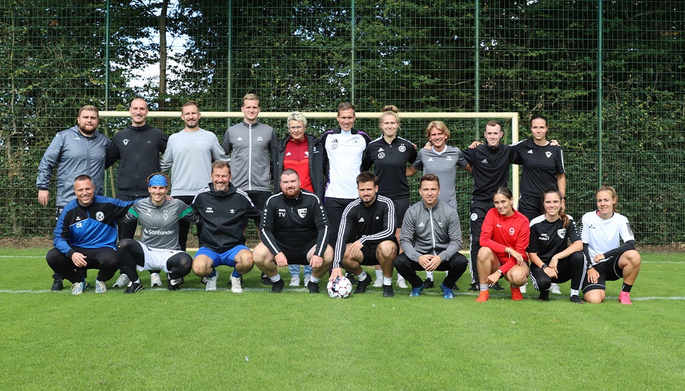 [{"clang_id":1,"value":"Fußballmannschaft und Betreuer auf grünem Rasen vor Metallzaun. Tragen Trainingskleidung, einige knien in der ersten Reihe. Ein Fußball liegt im Mittelpunkt."}]