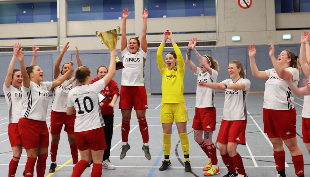 [{"clang_id":1,"value":"Frauenfußballteam jubelt in Sporthalle. Spielerinnen mit weiß-roten Trikots und rote Shorts heben Pokal hoch, einige springen."}]