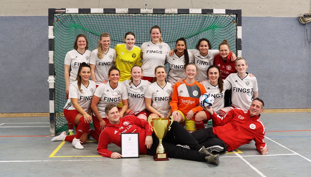 [{"clang_id":1,"value":"Handballteam vor Tornetz. Spielerinnen und Trainer in weißen und roten Trainingsanzügen mit Pokalen und Urkunde."}]