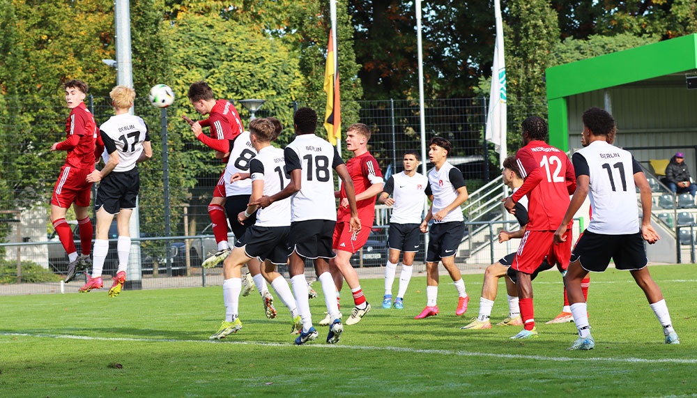 [{"clang_id":1,"value":"Fußballspiel: Zwei Mannschaften mit roten und weißen Trikots kämpfen um den Ball. Einige Spieler springen hoch, um den Ball zu köpfen. Im Hintergrund Zuschauer und Flaggen."}]