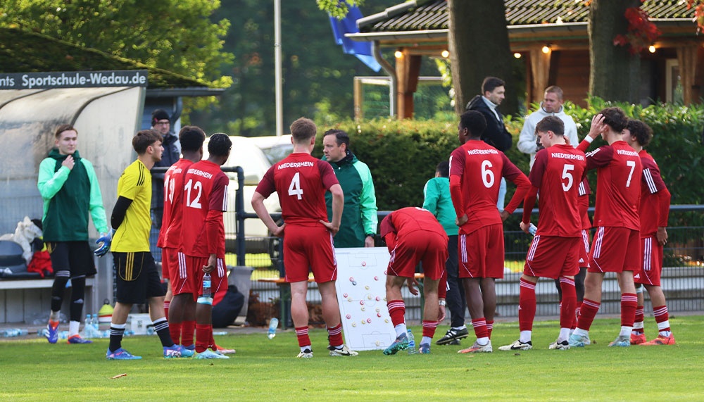 [{"clang_id":1,"value":"Fußballteam in roten Trikots und einige Spieler mit gelben Trikots stehen auf dem Rasen zusammen, diskutieren Taktik mit Trainer und Betreuer."}]