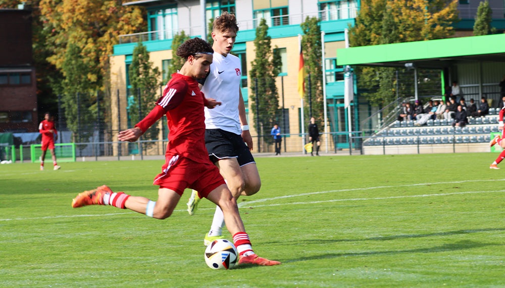 [{"clang_id":1,"value":"Zwei Fußballspieler im Spiel. Ein Spieler in Rot schießt auf das Tor, ein Spieler in Weiß verteidigt. Hintergrund: Fußballfeld und Gebäude."}]